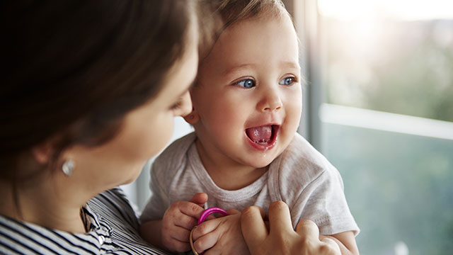 Lächelndes Baby wird von seiner Mutter gehalten