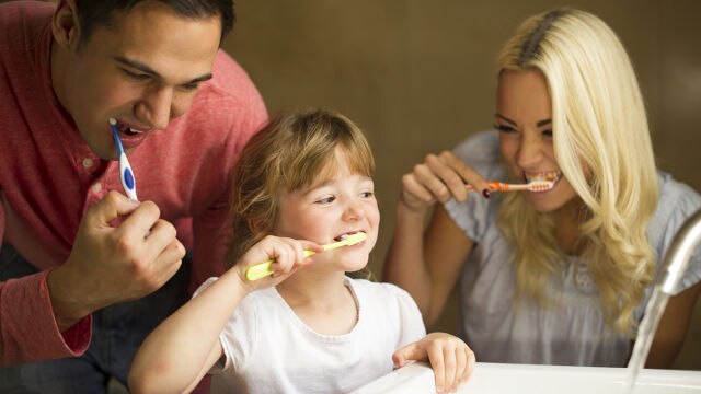 Familie mit Vater, Mutter und Kind putzt gemeinsam die Zähne im Badezimmer