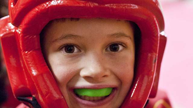 Kind mit rotem Helm und grünem Mundschutz beim Kampfsporttraining